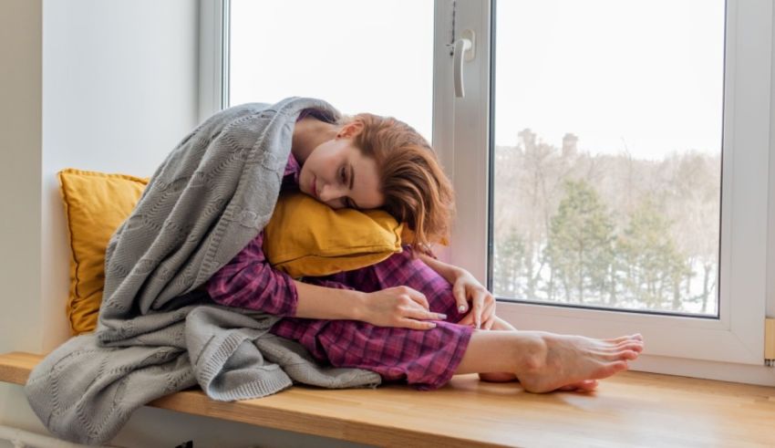 A woman is sitting on a window sill with a blanket over her head.