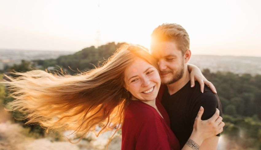 A man and woman hugging in front of a city at sunset.