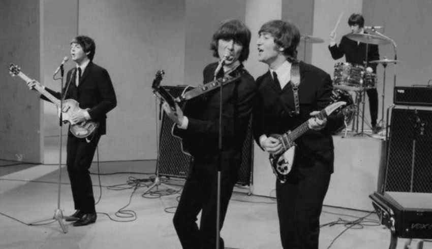 The beatles on stage with guitars and microphones.