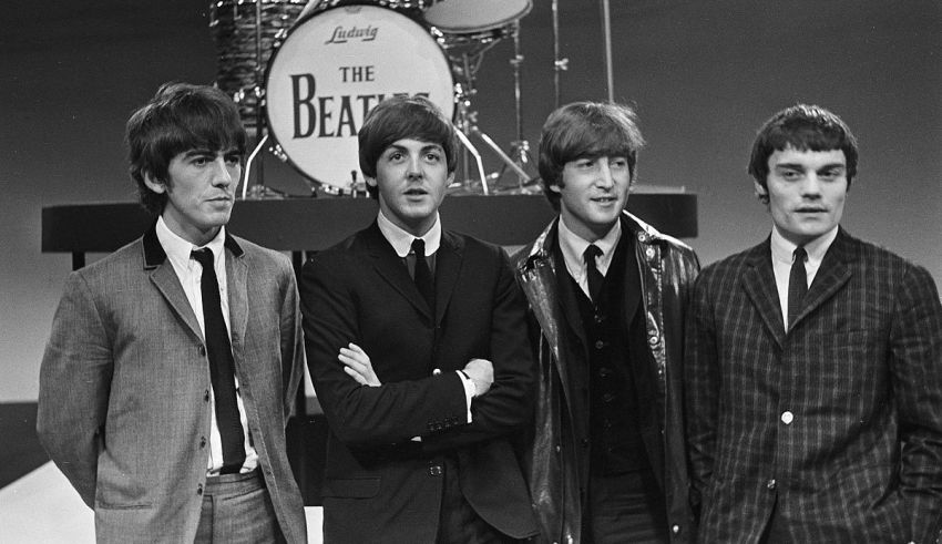 The beatles are posing in front of a drum set.