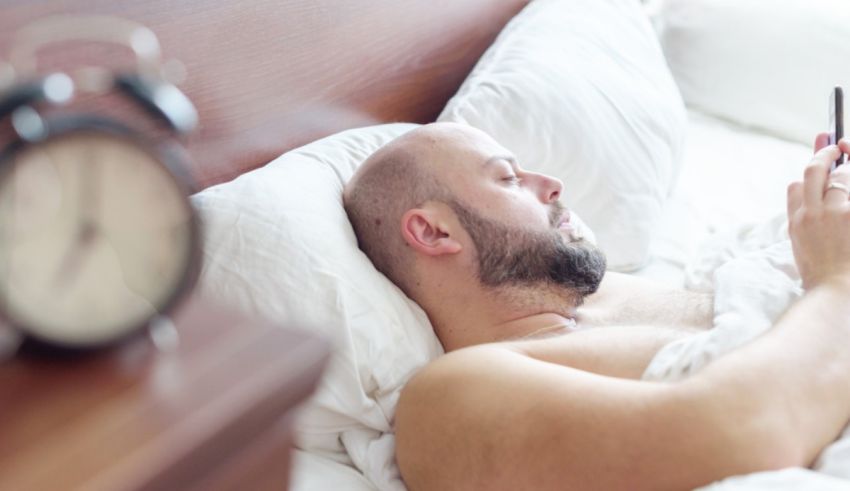 A man is lying in bed with a cell phone in his hand.