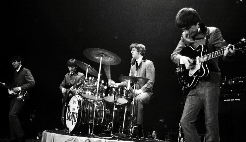 The beatles on stage with guitars and drums.