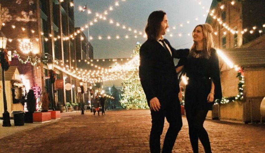 A couple standing in front of a brick walkway with christmas lights.