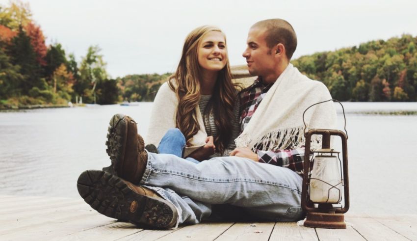 A couple sitting on a dock near a lake.