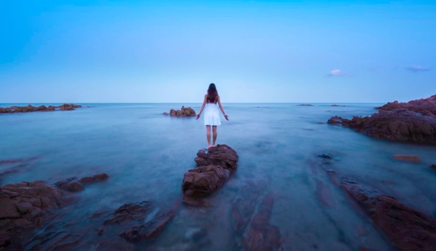 A woman is standing on a rock in the ocean.