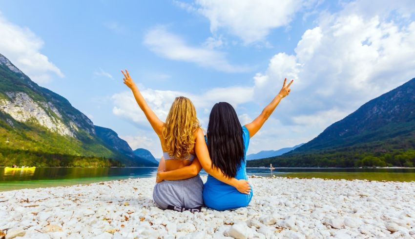 Two women sitting on a rock with their hands raised in the air.