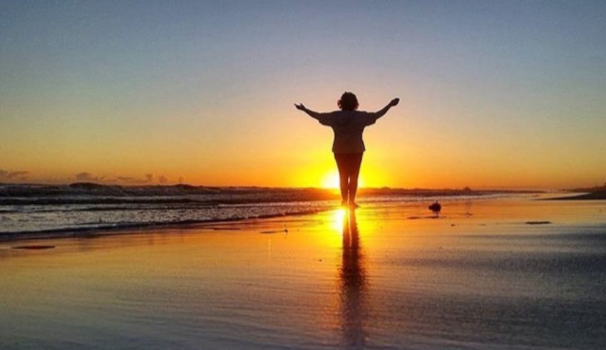 A woman standing on a beach with her arms outstretched.