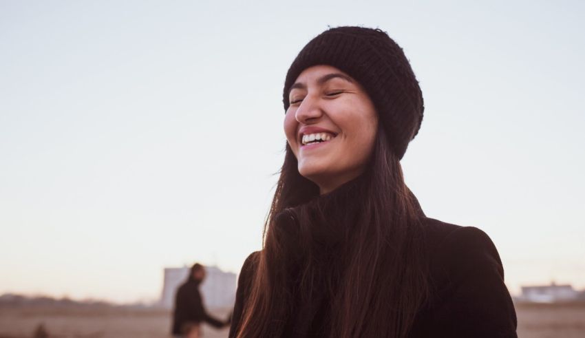 A woman wearing a black hat and a black jacket is smiling.
