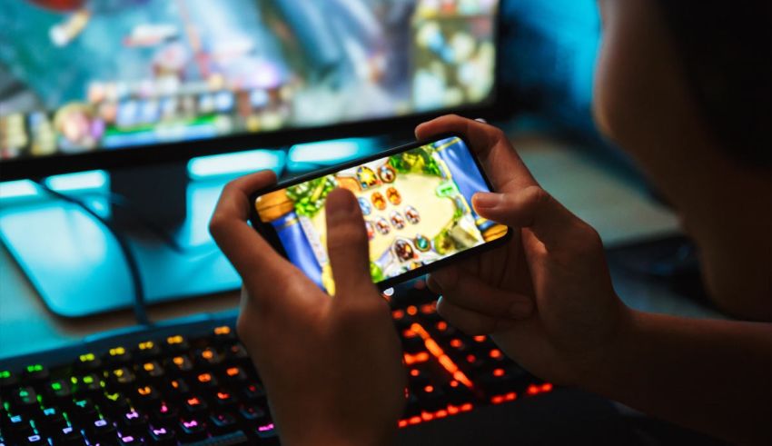 A person playing a game on a smartphone in front of a computer.