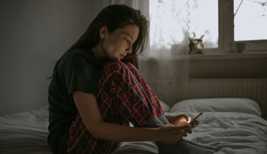 A woman in pajamas sitting on a bed looking at her phone.