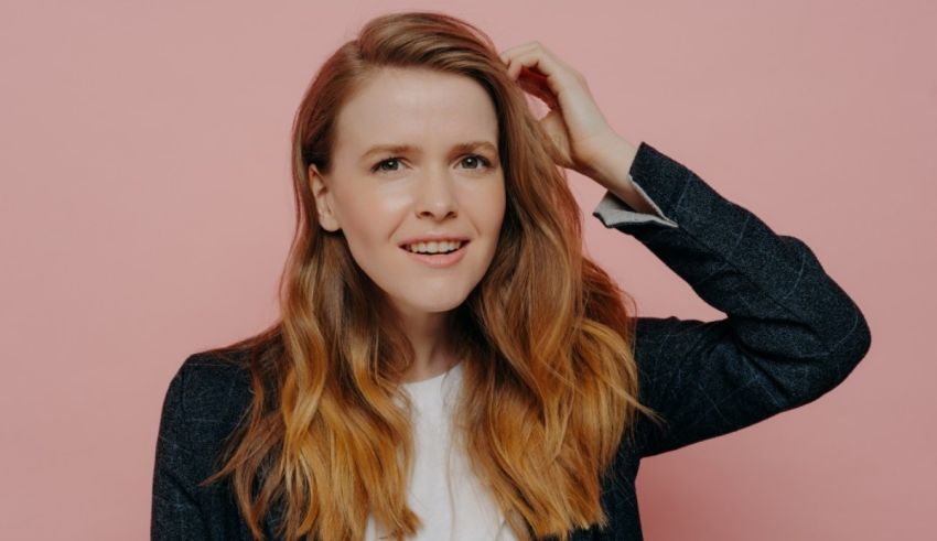 A woman with long hair posing against a pink background.