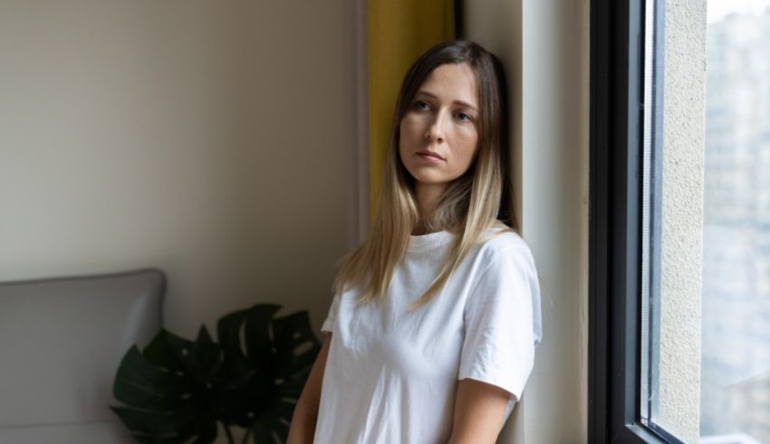 A woman in a white t - shirt is leaning against a window.