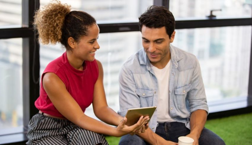 A man and woman sitting on the floor looking at a tablet computer.