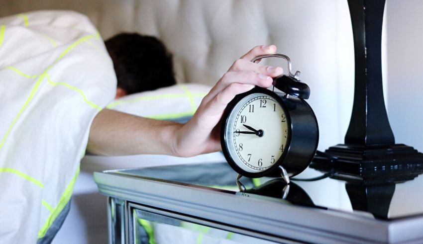 A man is laying in bed with an alarm clock.