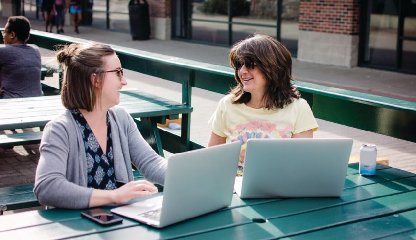 Two women sitting at a table with laptops.