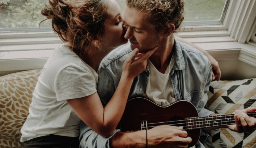 A couple kissing while holding an ukulele in front of a window.