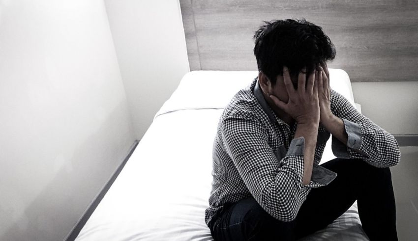 A man sitting on a bed with his hands on his face.