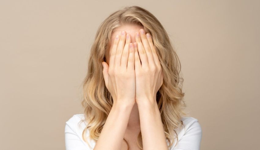 A woman covering her eyes with her hands on a beige background.