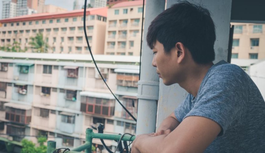 A young asian man sitting on a balcony overlooking a city.