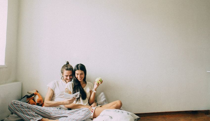A man and woman sitting on a bed in a room.