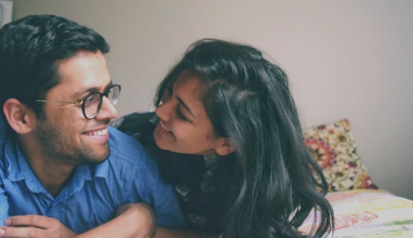 A man and woman are laying on a bed and smiling.