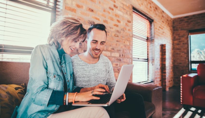A man and woman sitting on a couch using a laptop.