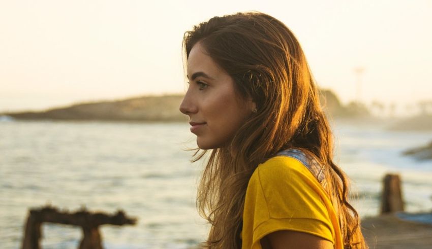 A young woman looking at the ocean with headphones on.