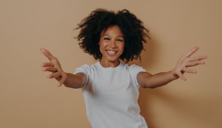 Young african american woman posing with arms outstretched on a beige background.