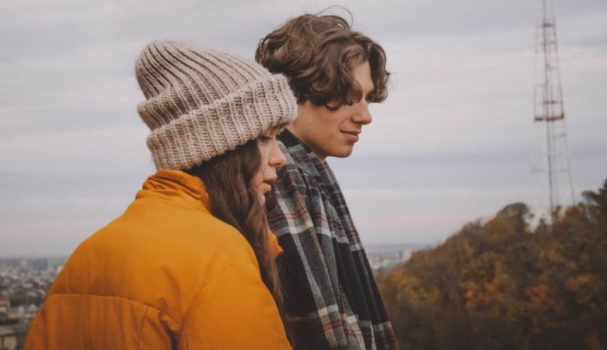 A couple looking at each other while standing on top of a hill.