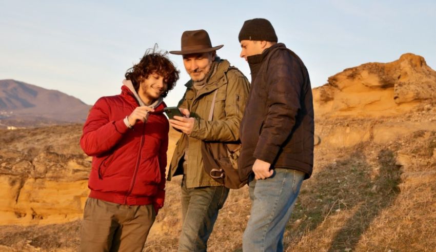 Three men are standing in a field looking at a cell phone.