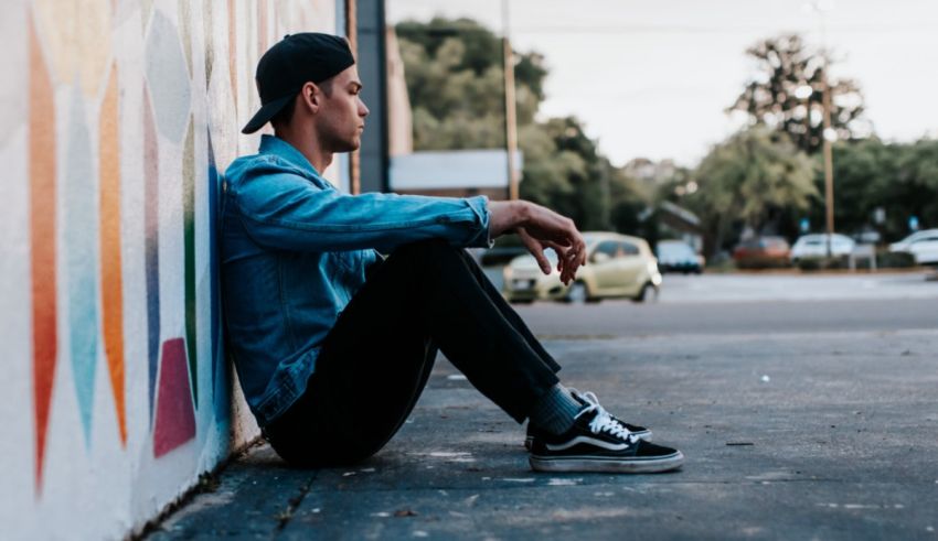 A young man sitting on the side of a wall with graffiti.