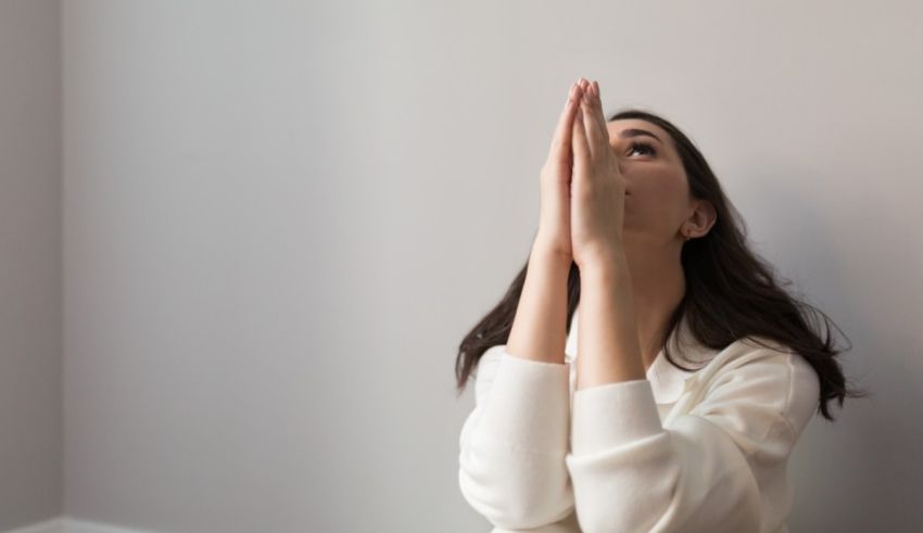 A young woman praying in front of a gray wall.