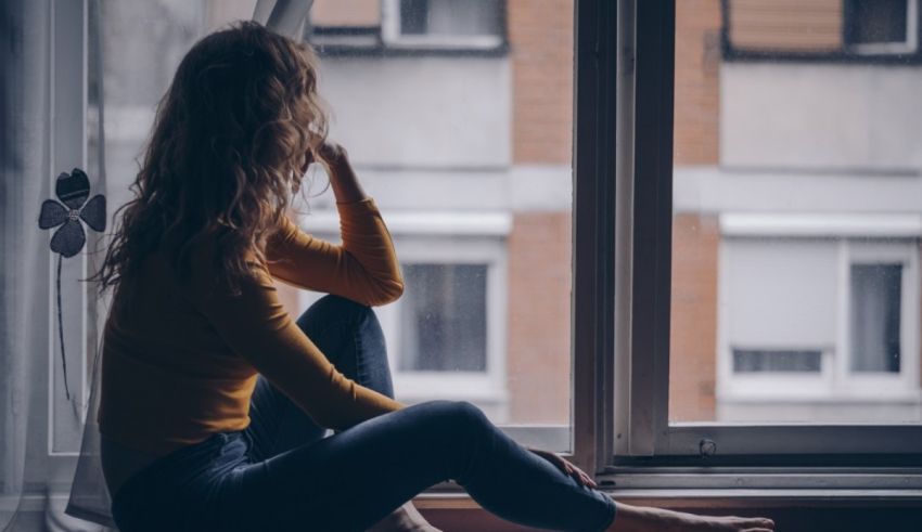 A woman sitting on a window sill looking out.
