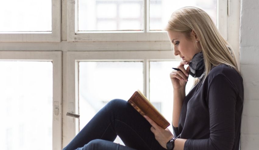 A woman is sitting on a window sill reading a book.