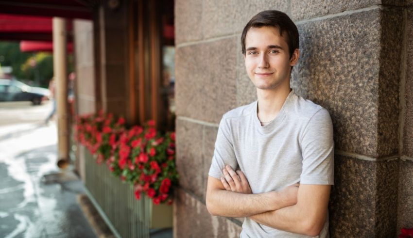 A young man leaning against a wall with his arms crossed.