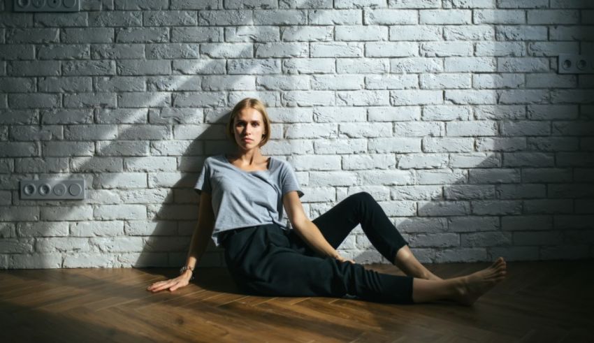 A young woman sitting on the floor in front of a brick wall.