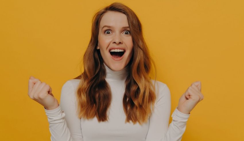 A woman with her arms up in the air on a yellow background.