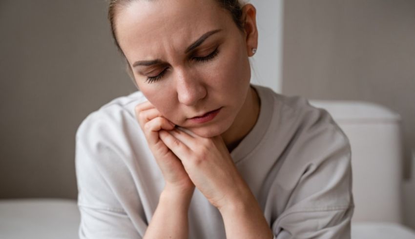 A woman with a toothache is sitting on a bed.