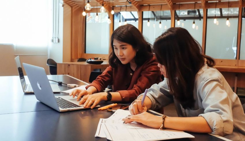 Two women working on laptops in a conference room.