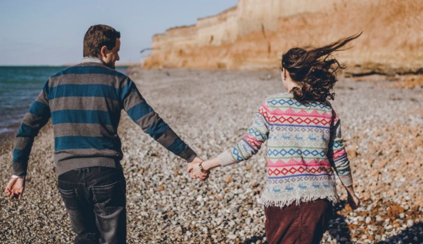 A couple holding hands while walking on the beach.
