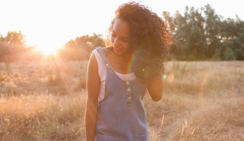A woman in overalls standing in a field at sunset.