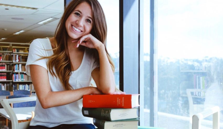 A young woman sitting in a library with a stack of books.