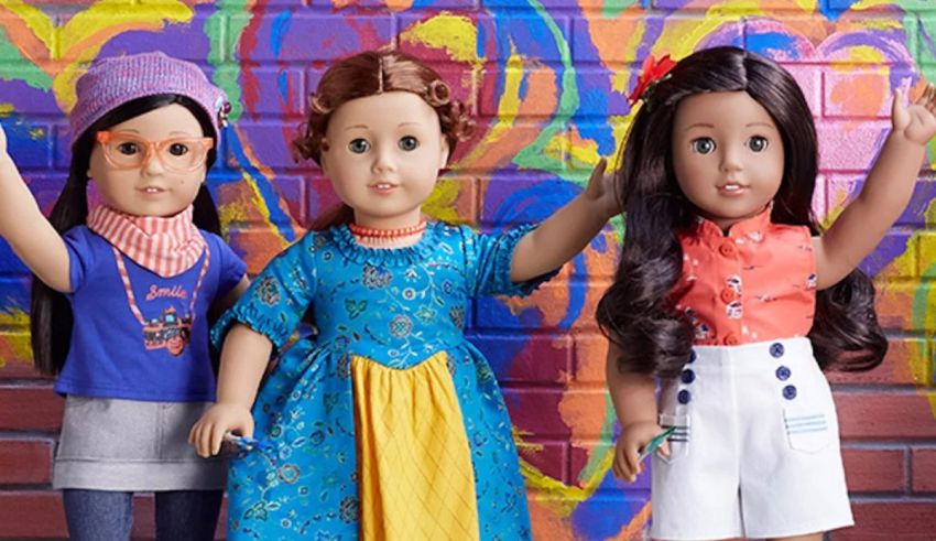 Three american girl dolls standing in front of a colorful wall.