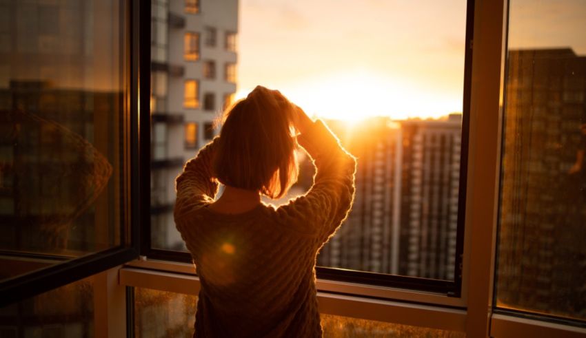 A woman looking out of a window at sunset.