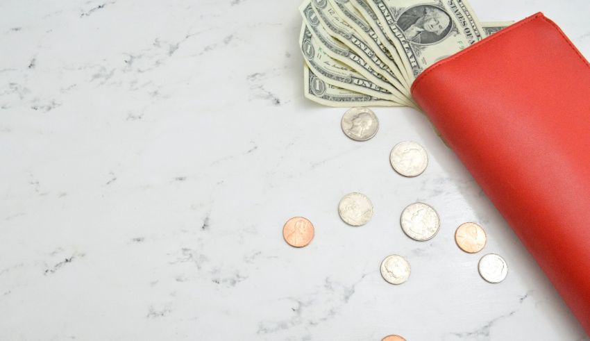 A red wallet with money and coins on a marble table.
