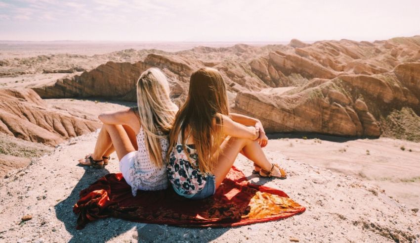 Two women sitting on top of a rock in a desert.