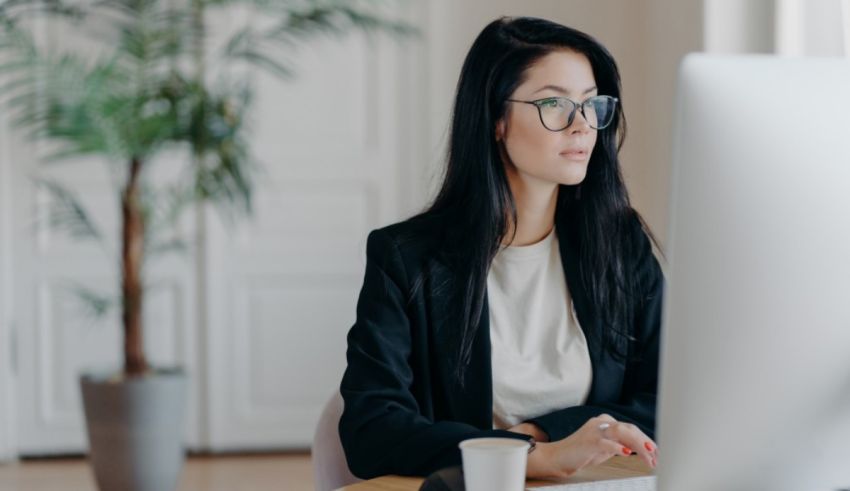 A woman wearing glasses is sitting at a desk in front of a computer.