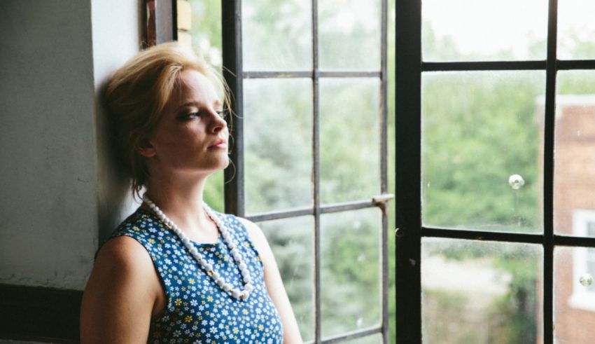 A woman looking out a window in a blue dress.