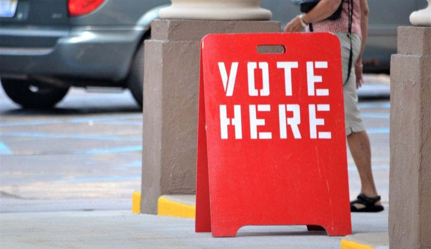A red sign that says vote here in front of a car.