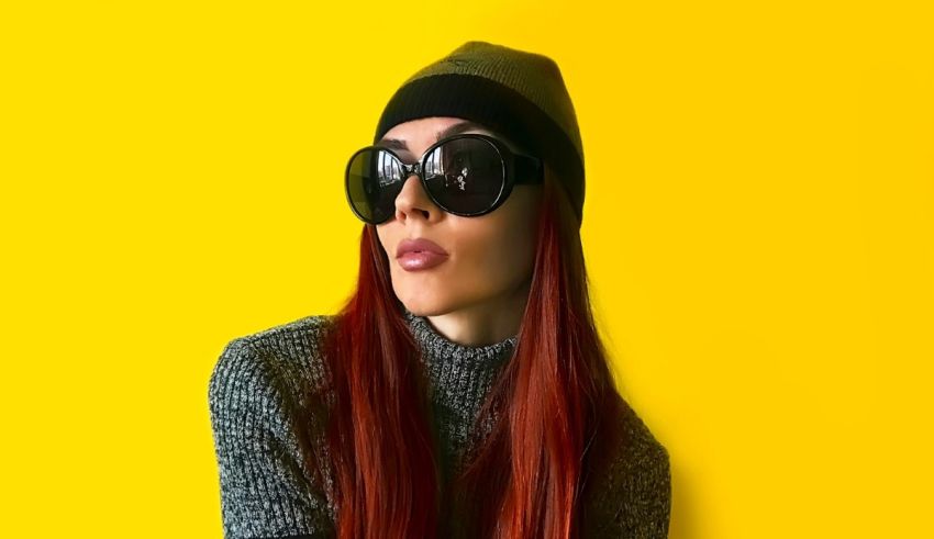A woman wearing sunglasses and a beanie on a yellow background.